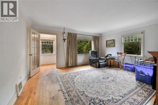 Spacious living room with large windows, wooden floors, a patterned rug, and a recliner. - 482 Ker Ave, Saanich