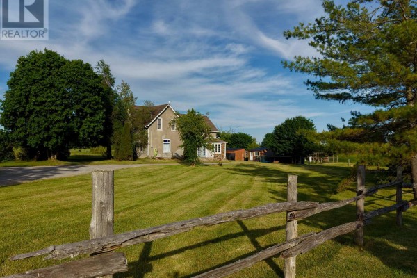 Distant view of the house across a green lawn with a wooden fence in the foreground. - 482 Portage Road, Kawartha Lakes