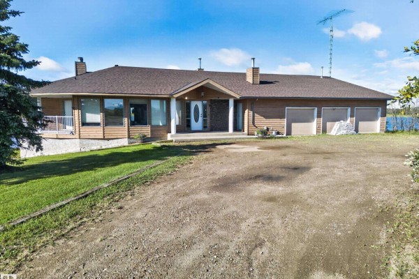 Front view of a long, single-story home with a three-car garage, stone pillars, and a circular driveway. - 48208 Range Road, Rural Beaver County