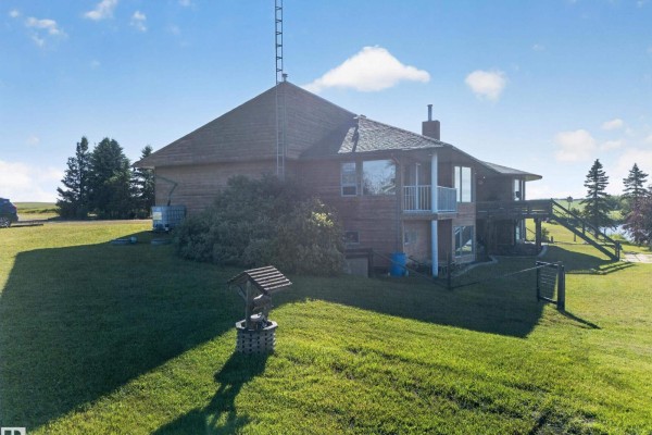 Side view of a home with a well, large windows, a balcony, and extensive green space surrounding the property. - 48208 Range Road, Rural Beaver County