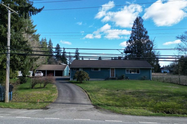 Front view of a single-story green house with a brown roof and yard. - 4824 248 Street, Langley