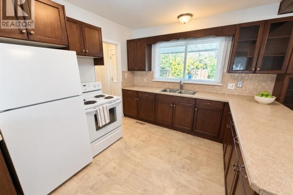 Kitchen with dark wood cabinets, white refrigerator, white stove, and a window view. - 4825 51 Avenue, Taber