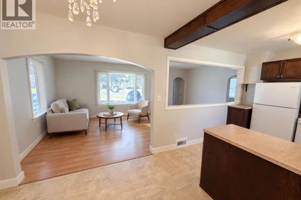 Living room with a sofa and chairs, connected to the kitchen area by an archway. - 4825 51 Avenue, Taber