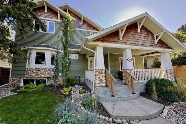 Exterior view of the house from the side, showing green siding and stone detailing on the porch columns. - 4825 Ada Bv Nw, Edmonton