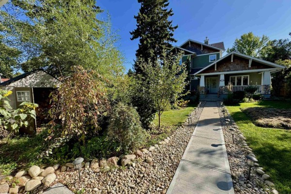 Side view of the house with surrounding trees, garden beds, and a small shed on the left. - 4825 Ada Bv Nw, Edmonton