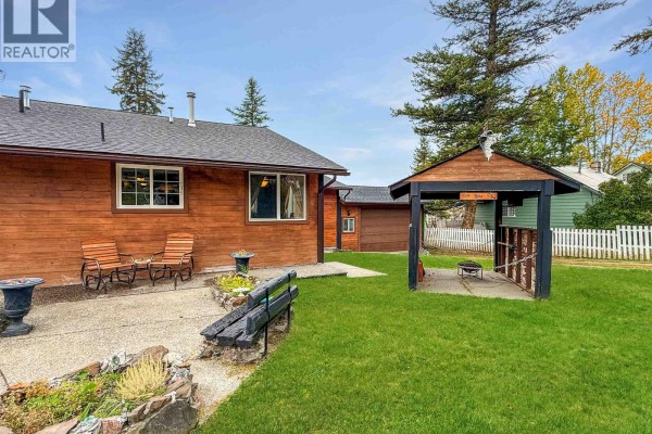 Backyard with green grass, seating area, and covered outdoor entertainment space. - 4832 Clarke Avenue, Lac La Hache
