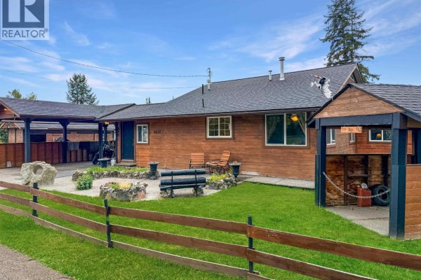 Front yard with fire pit, seating, grass, wooden fence, and house exterior. - 4832 Clarke Avenue, Lac La Hache