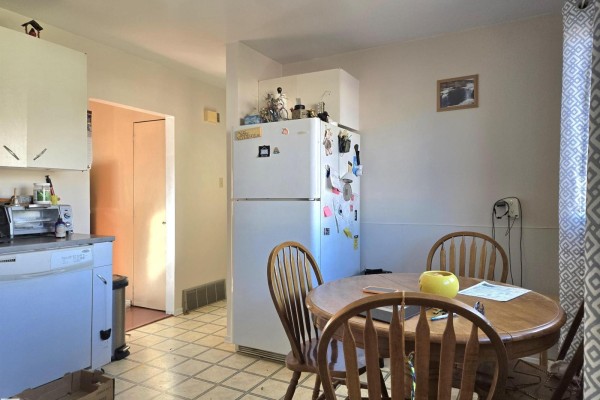 Kitchenette with a round wooden table and chairs next to a white refrigerator. - 4835 47 St, Thorsby