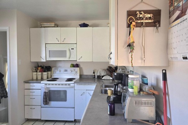White kitchen cabinets, stovetop, microwave, and sink with grey countertops. - 4835 47 St, Thorsby