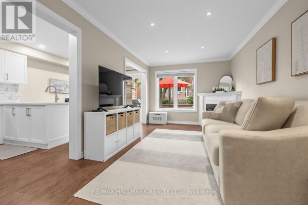 Living room with a beige sofa, fireplace, television, and view of the kitchen area. - 484 Bartholemew Drive, Newmarket