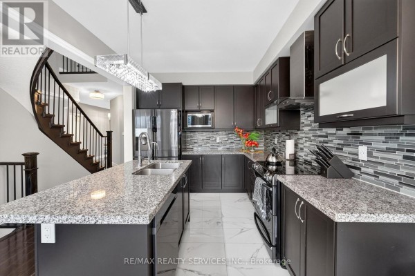 Modern kitchen with granite island, dark cabinets, mosaic backsplash & curved stairs - 484 Greenwood Drive Essa