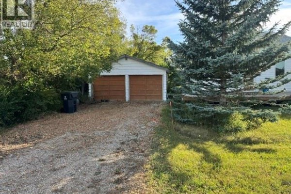 Exterior view of a white garage with two wooden doors and a gravel driveway. - 485 3rd Avenue, Lajord Rm No  128