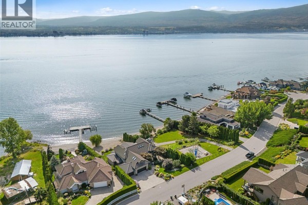 Exterior view of a modern home with large glass balcony, landscaped lawn, and surrounding trees. - 485 Casa Rio Drive, West Kelowna
