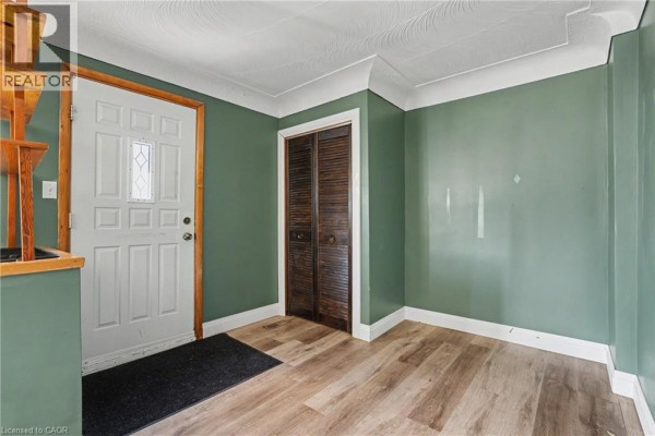 Entranceway of a home with green walls, white door, wooden closet doors, and light wood laminate flooring. - 485 Cochrane Road, Hamilton