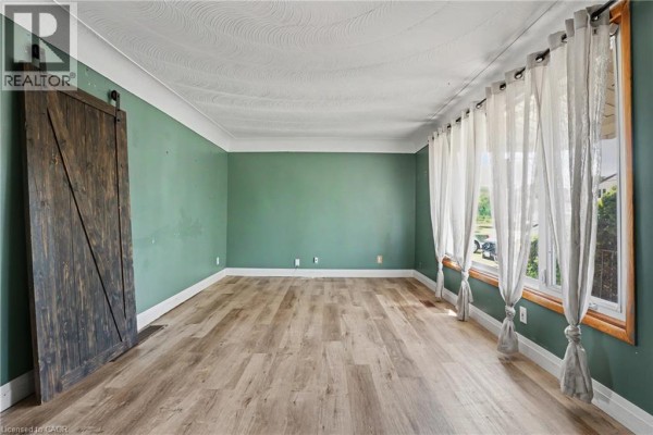 Living room with green walls, light wood laminate flooring, white curtains, and a large wooden barn door. - 485 Cochrane Road, Hamilton