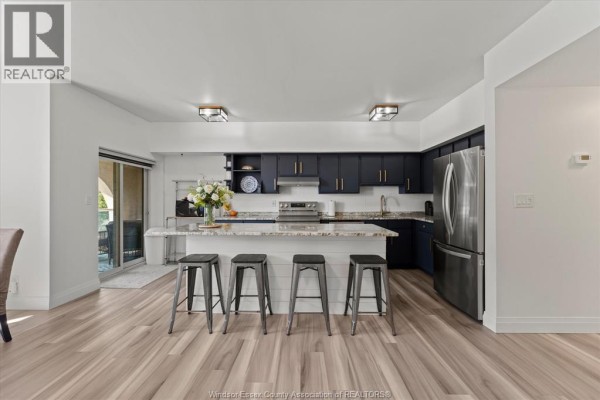 Close-up of kitchen with dark blue cabinets, white subway tile backsplash, granite countertops, and stainless steel appliances. - 4850 Grand Boulevard Unit# 306, Windsor