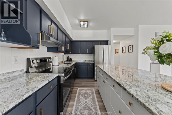 Kitchen view showing stainless steel appliances, dark blue cabinets, granite countertops, and sliding glass door to balcony. - 4850 Grand Boulevard Unit# 306, Windsor