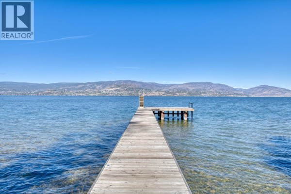 Wooden dock extending into clear blue water with mountains in the distance. - 4852-4858 Lakeshore Road, Kelowna
