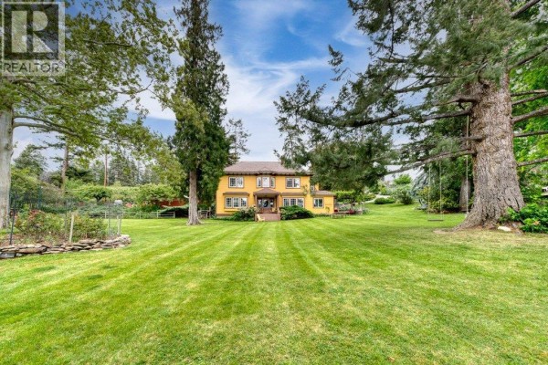 Yellow two-story house with large green lawn and mature trees on a sunny day. - 4852-4858 Lakeshore Road, Kelowna