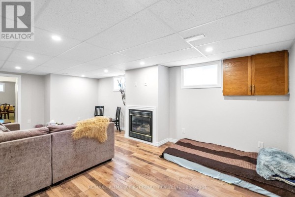 Basement living space featuring a sectional sofa, fireplace, and a mattress on the floor. - 487 Cunningham Avenue, Oshawa