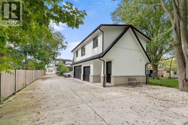 Long concrete driveway leading to a two-story white house with black trim and garage doors. - 487 Dalhousie Street, Amherstburg