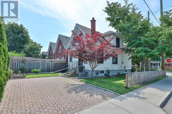 Rear view of the house with a red brick chimney, white siding, paved driveway, and picket fence. - 487 Dunsmure Road, Hamilton