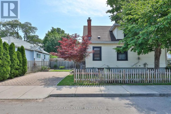 Side and rear exterior view of the house with white siding, red brick chimney, paved driveway, and fence. - 487 Dunsmure Road, Hamilton