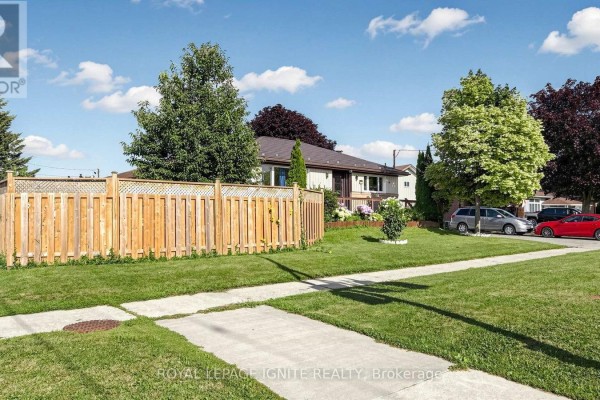 Side view of a beige and cream bungalow with a wooden fence and mature trees. - 487 Wilson Road S, Oshawa