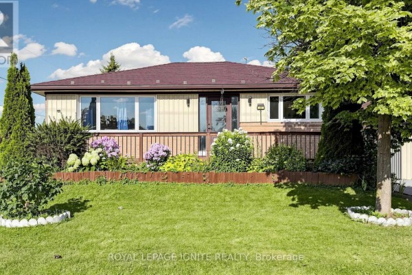 Front exterior of a beige and cream bungalow with a dark brown roof, porch, and flower beds. - 487 Wilson Road S, Oshawa