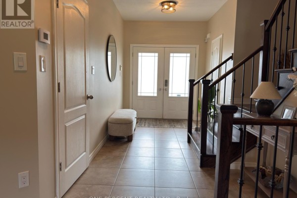 Tiled entryway with double glass doors, a bench, and a staircase with dark wood railings. - 4871 Northgate Crescent, Lincoln
