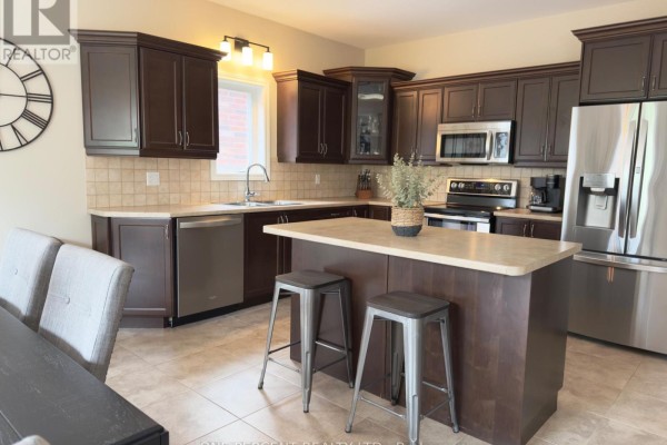 Kitchen with dark wood cabinets, stainless steel appliances, a kitchen island with stools, and tile flooring. - 4871 Northgate Crescent, Lincoln