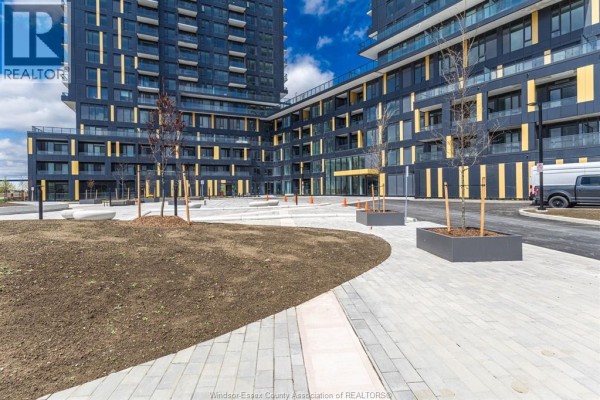 Courtyard area with paved walkways, planters, and modern apartment building exterior in the background. - 4878 Powers Common, Burlington