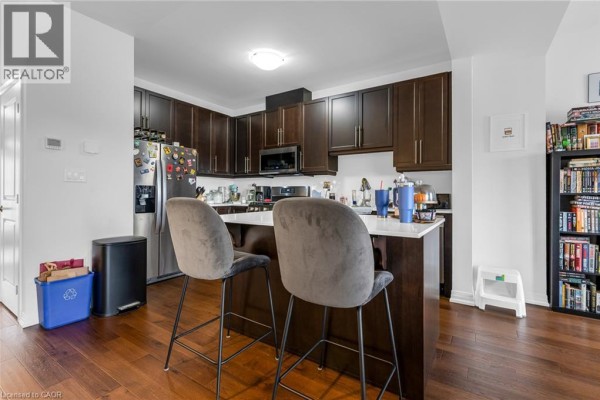 Kitchen island with two upholstered stools, dark wood cabinets, stainless steel refrigerator and microwave. - 4879 Connor Drive, Beamsville