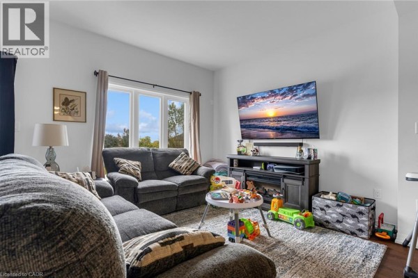 Living room with a large sectional sofa, television, fireplace, and a bay window overlooking greenery. - 4879 Connor Drive, Beamsville