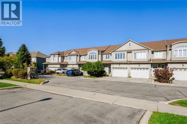 Exterior view of beige townhouses with white garages and manicured landscaping on a sunny day. - 488 Stonehenge Drive, Ancaster