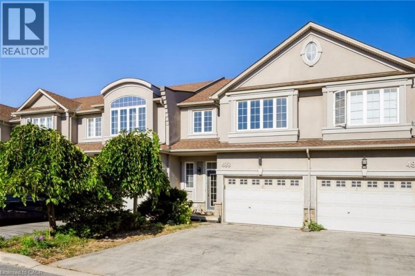 Close-up of two beige townhouses with arched windows, white trim, and double garages. - 488 Stonehenge Drive, Ancaster