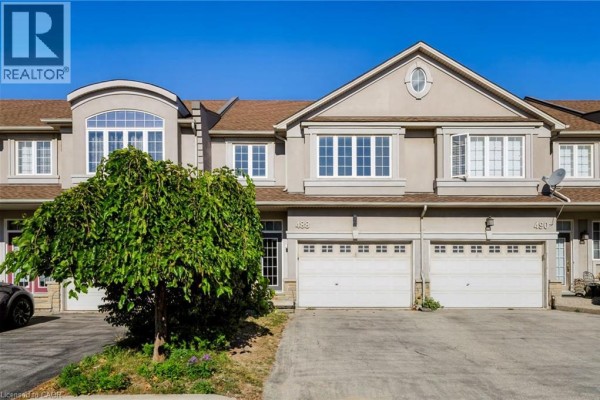 Front exterior of beige townhouses featuring white windows, garages, and a weeping tree. - 488 Stonehenge Drive, Ancaster
