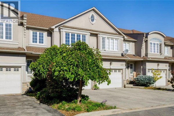Facade of beige townhouses with multiple windows, white garages, and green landscaping. - 488 Stonehenge Drive, Ancaster