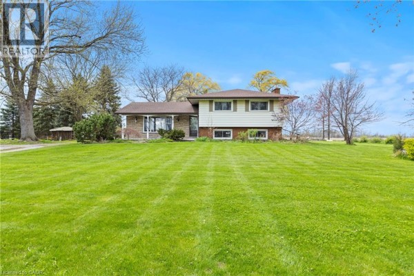Exterior of a split-level home with a long, manicured lawn and mature trees under a clear blue sky. - 488 Townline Road, Niagara On The Lake