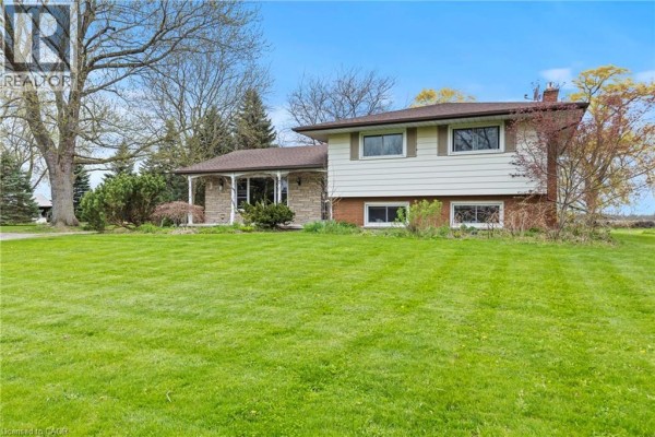 Side view of a split-level house showing its brick and vinyl exterior, surrounded by a green lawn and trees. - 488 Townline Road, Niagara On The Lake