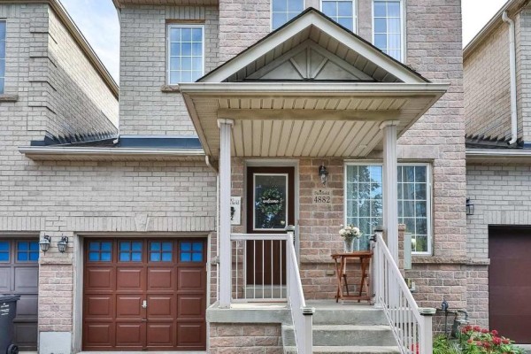 Close-up of the covered front entrance with brick detailing, white railings, and double garage doors. - 4882 Vienna Court, Mississauga