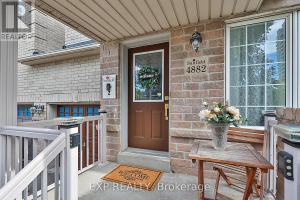 Front door with glass inserts and a welcome mat, flanked by windows and brick exterior. - 4882 Vienna Court, Mississauga