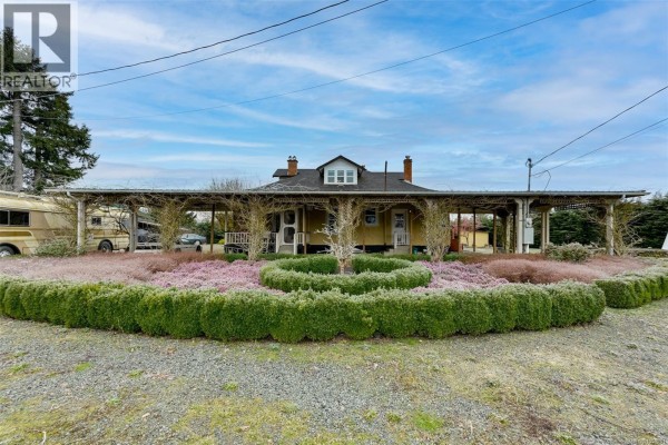 Open wrought iron gates on stone pillars leading to a gravel driveway and rural property. - 4890 Wilson Rd, Duncan