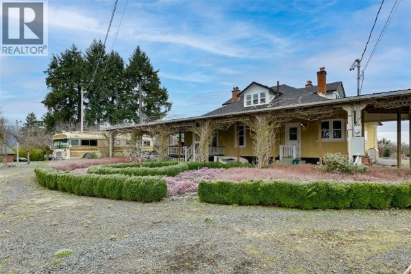 Covered front porch with wooden floorboards, yellow siding, and a wooden front door. - 4890 Wilson Rd, Duncan
