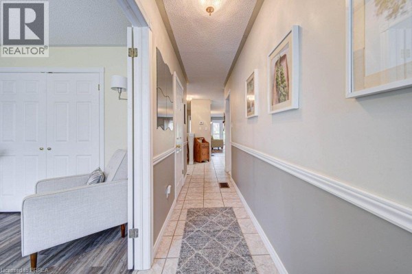 Hallway interior with tiled floor, beige walls, wainscoting, and artwork on walls. - 48c Harris Avenue, Brantford
