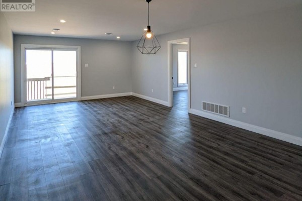Open concept living and dining area with grey walls, dark wood floors, and sliding glass doors. - 49 - 55 Adam Street, The Nation