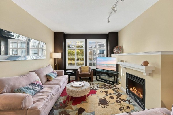 Living room with a fireplace, pink sofa, armchair, television, and large floral rug. - 49 18828 69 Avenue, Surrey