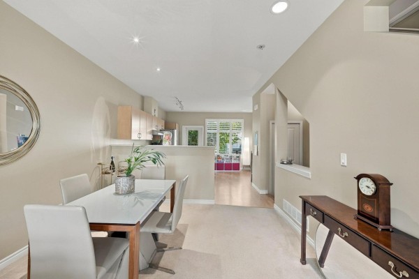 Dining area with a glass-top table, white chairs, and a view towards the kitchen and living room. - 49 18828 69 Avenue, Surrey