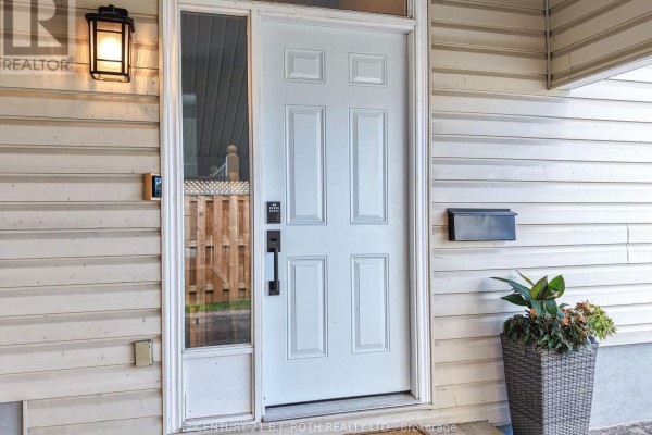 White front door with glass sidelight and black hardware, next to a planter. - 49 Bond Street, Orillia