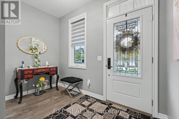 Interior foyer with light grey walls, wood-look flooring, a white front door with stained glass, and a small vanity table. - 49 Campbell Street, Thorold